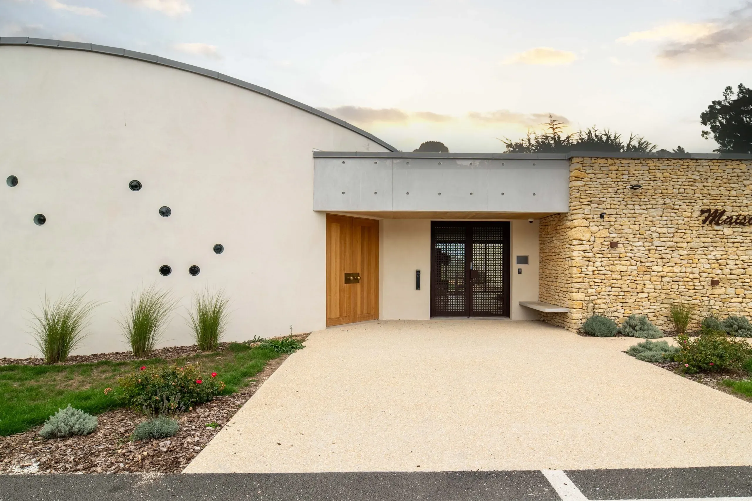 Façade moderne de la maison funéraire en pierres apparentes et crépi blanc avec chemin d'accès